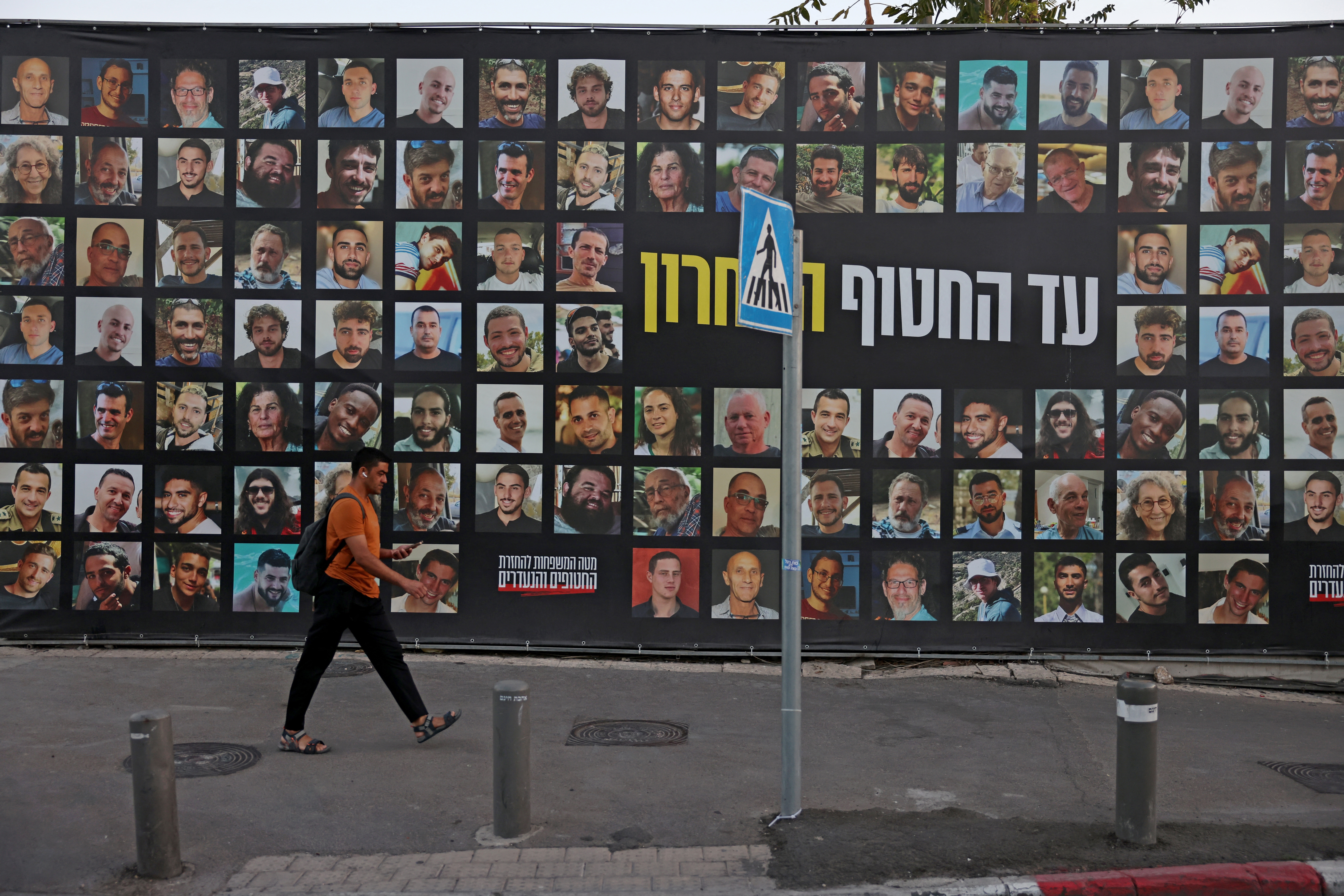 A man walks past a billboard bearing the portraits of Israelis held hostage in the Gaza Strip by Palestinian militants since Oct.2023.